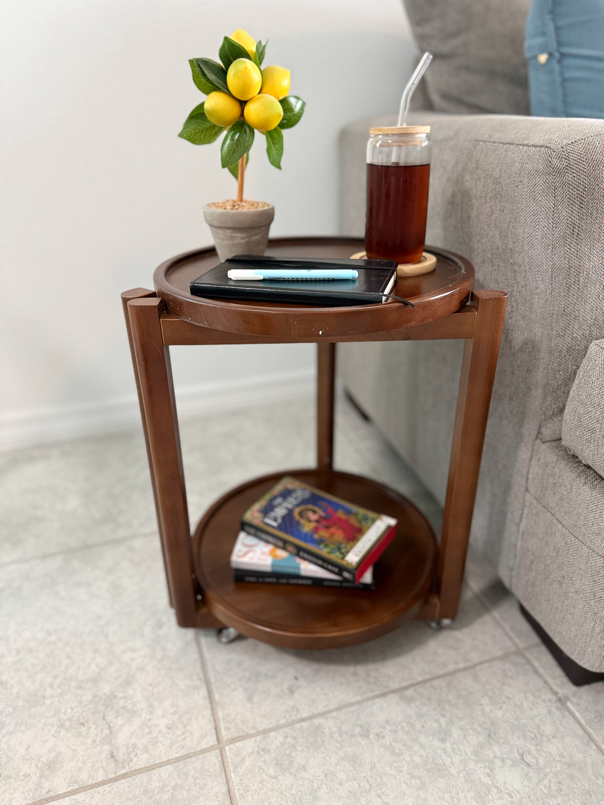 Taitiy solid wood side table styled with drinks and books next to a couch in a living room